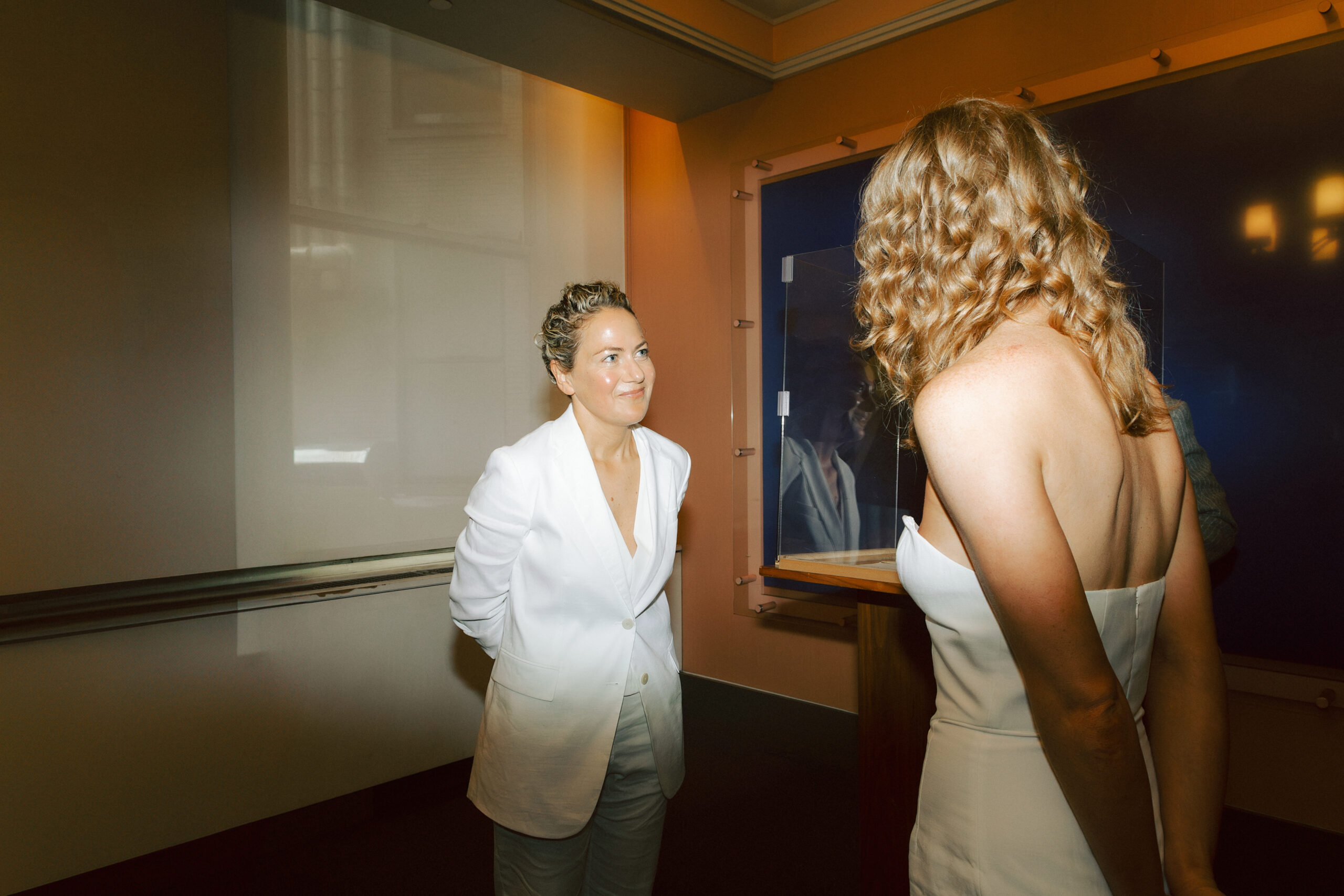 Civil ceremony at the NYC city Hall between Jane, sporting a white jumpsuit, and Catie in a white dress.