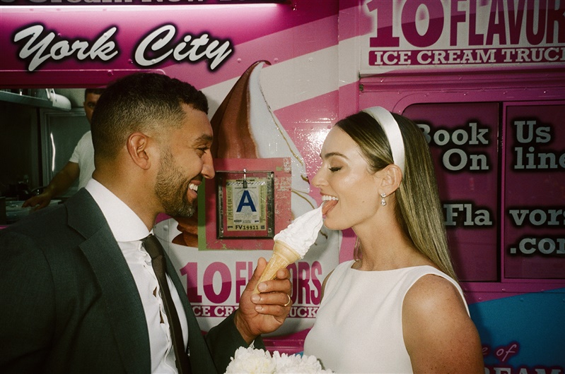 Groom sharing a bite of ice cream cone with bride in front of NYC ice cream truck