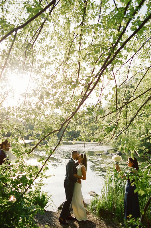 Bride and groom sharing their first kiss through the trees during Prospect Park wedding.