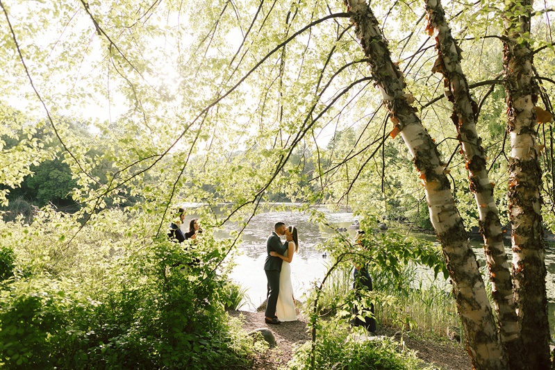 Bride and groom photo sharing first kiss at Prospect Park wedding ceremony, shot with trees framing the couple.