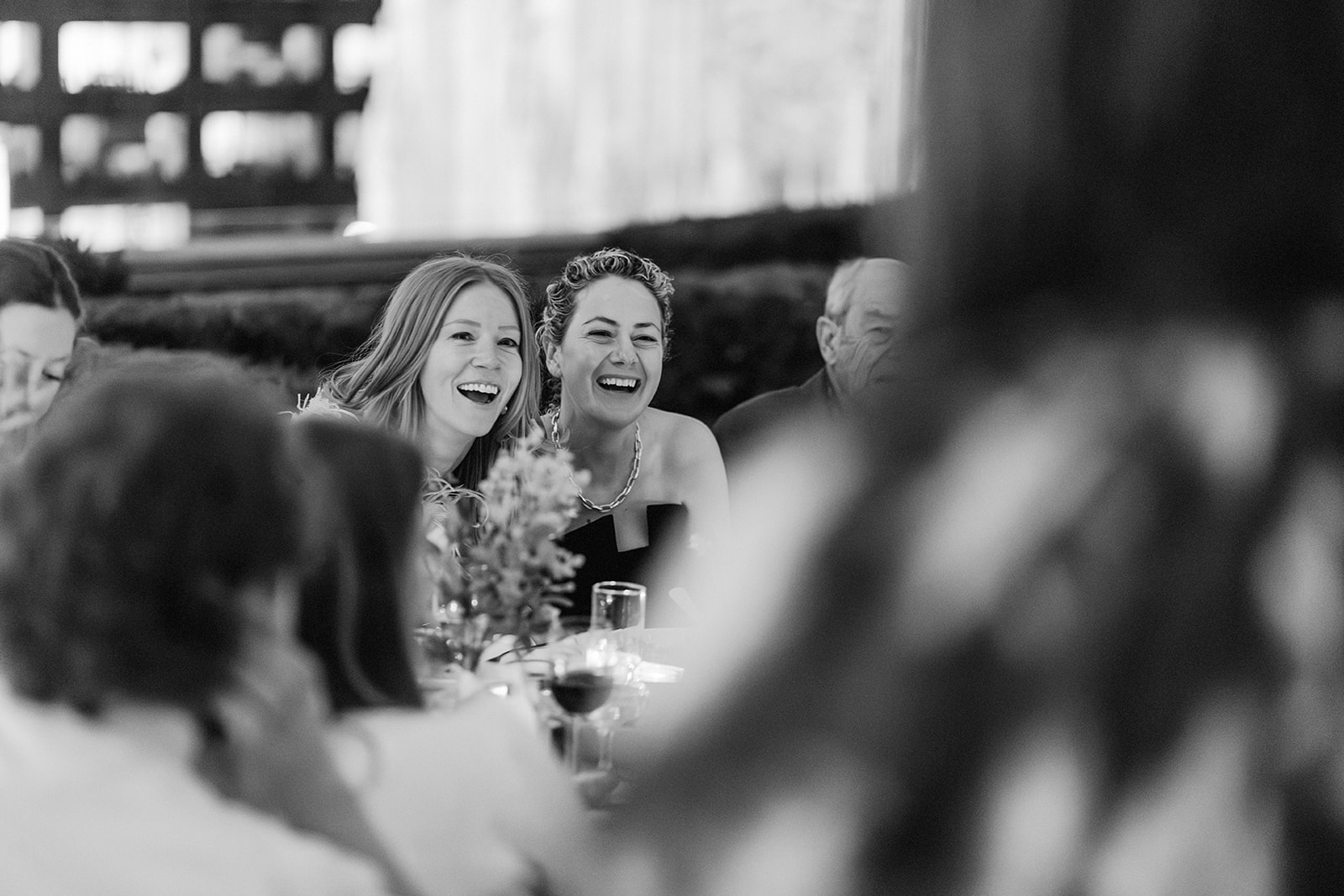Couple listening to toasts at their wedding dinner in a black and white photo of blur around them but focusing on the couple's faces