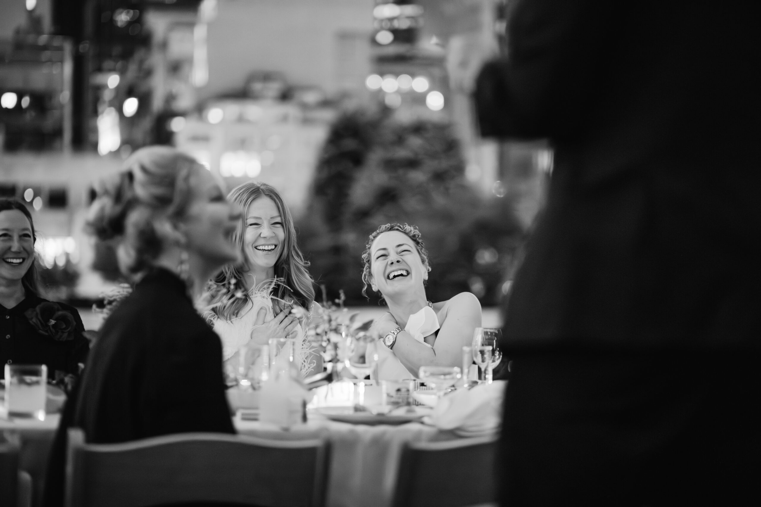 Black and white wedding reception photo of couple laughing during their toasts