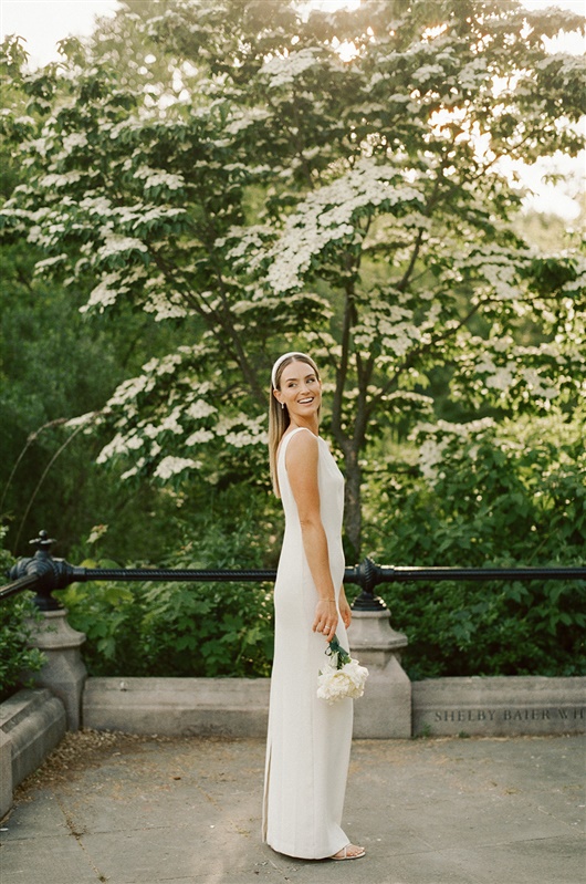 Bride looking over her shoulder for a photo in her elopement dress posing in front of green and white trees