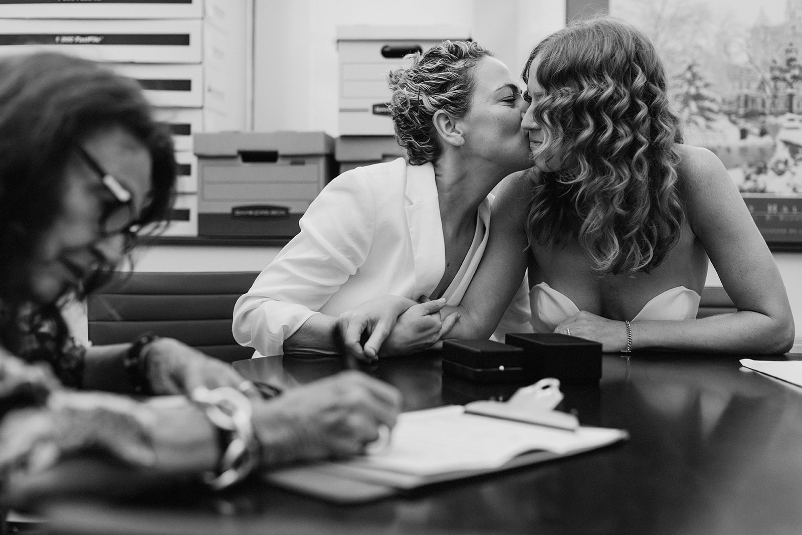Fashion icon Diane von Furstenberg signing a marriage license at the New York City courthouse elopement for Catie and Jane while the couple shares a cheek kiss in the background