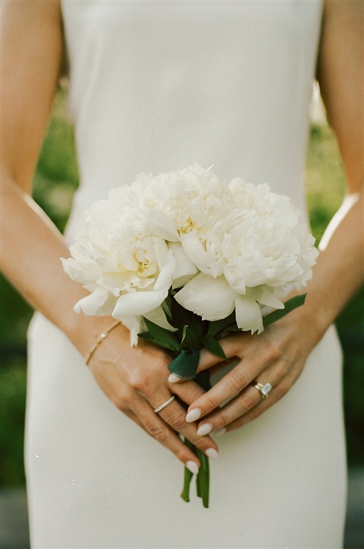 Bride's wedding flowers and ring detail shot of white wedding bouquet