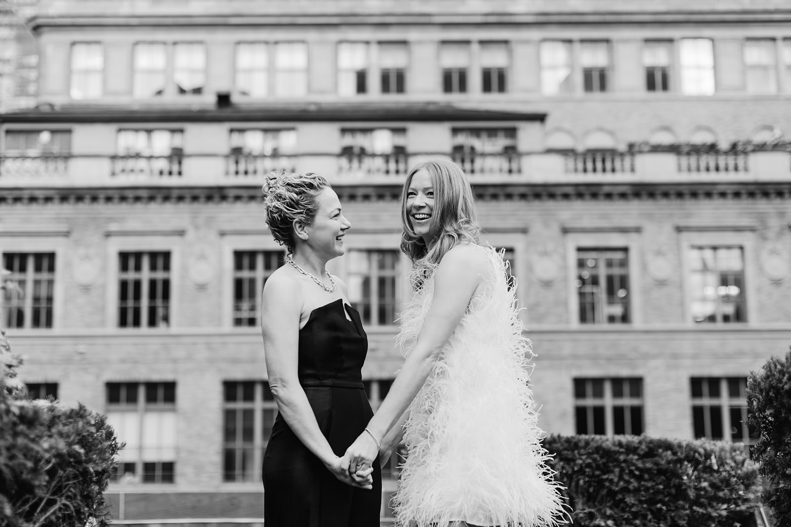 Same sex couple wedding reception outfits with one bride in a black jumpsuit and another in a mini feather dress